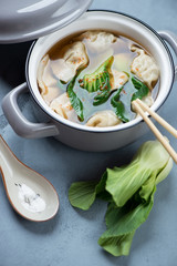Miso soup with wontons and bok choy in a pan, vertical shot over grey concrete background, elevated view