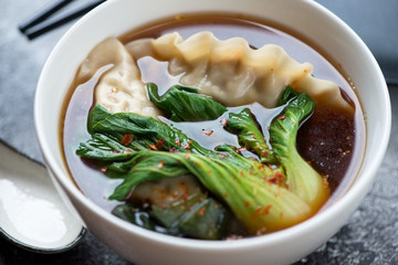 Closeup of miso soup with dumplings and pak-choi served in a white bowl, selective focus