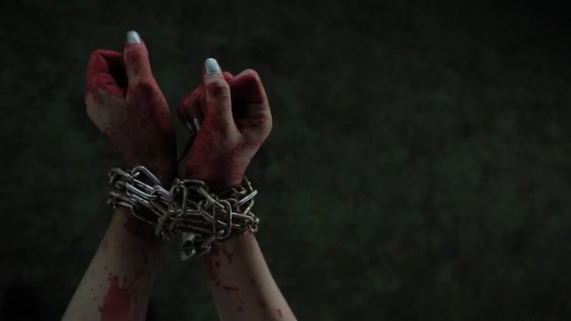 Bound hands of lady with nail fashion, kidnap for money. Tie hands with metal chain mess with blood on dirty background, she try to force it to release then give up