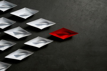 Business Concept,, key opinion Leader, the concept of influence. One red paper boat as the Leader, leading in the direction of the white ships on a gray concrete background,copy space,flat lay
