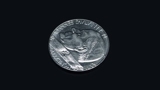 Coin IOANNES PAVLVS II P M A VII MCMLXXXV citta del vaticano 100 lire rotates on a black background. Macro. Closeup