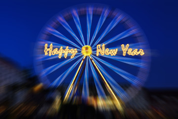 Happy New Year sparkling text over a spinning ferris wheel in motion blur against a dark blue sky, copy space