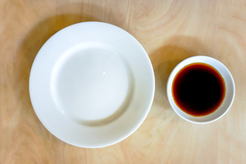 A blank white plate with a Soy sauce on a wooden desk.