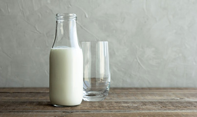 A glass bottle with kefir, milk or homemade fresh yogurt stands on a rustic table and next to it is an empty glass cup. Kefir is a healthy snack and it is rich in prebiotics.
