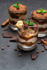 Classic tiramisu dessert in a glass cup and pieces of chocolate on dark concrete background