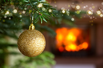 Golden Christmas ball against a stone fireplace. Bokeh holiday light background.