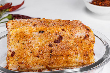A large piece of salted lard with paprika and hot pepper lies in a white plate on a white background