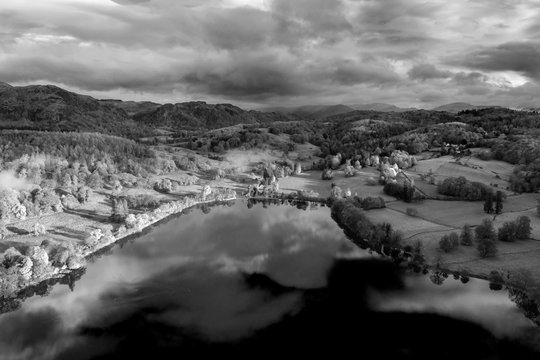 Breathtaking black and white aerial drone landscape images over Coniston Water at sunrise on beautiful Autumn Fall morning