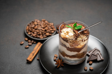 Classic tiramisu dessert in a glass cup and pieces of chocolate on dark concrete background