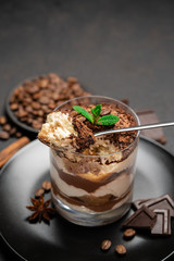 Classic tiramisu dessert in a glass cup and pieces of chocolate on dark concrete background