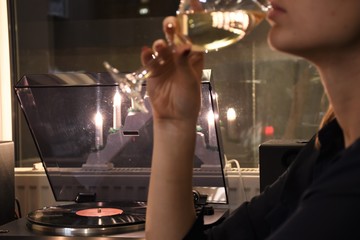 Girl with red nails and sensual lips drinking white wine with vinyl player and candles on background, relaxing and cozy atmosphere 