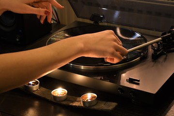 Beautiful hand of a girl with red nails playing a vinyl with light of candles
