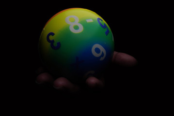 Small ball toys with hand is holding. Number pattern ball and dark background.