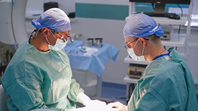 Doctors in medical uniform during the operation. Surgeons perform an operation on the background of medical instruments in the operating room.
