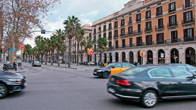 Unrecognized cars, taxis, cyclists and locals in the center of Barcelona, a crossroads with busy traffic. Boulevard with palm trees in the background