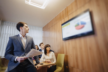 Meeting of office workers at the table, looking at the presentation with diagrams on the TV