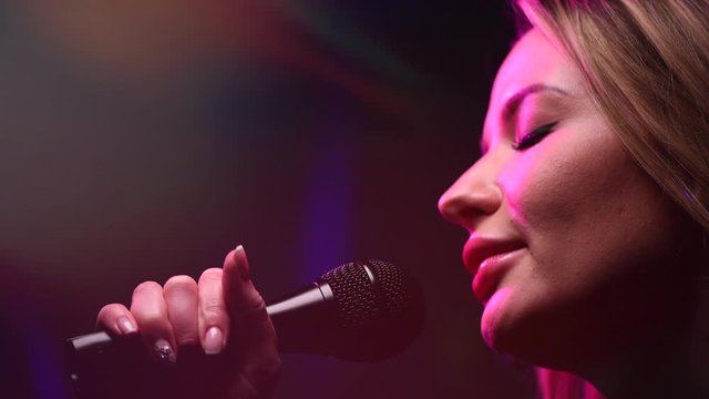 Singing Woman with Microphone. Karaoke bar. Beauty Glamour professional singer girl close-up. Stage. Rock star singer on music concert over colorful lights background. Song, music concept. 4K UHD