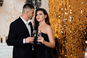 A bearded guy with a girl pose in a studio. Loving couple, is stylishly dressed near a Christmas tree. Christmas time. Christmas mood. Loving couple celebrating New Year and Christmas with champagne. 