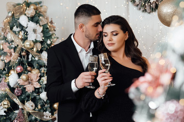 Beautiful couple holding champagne glasses. Lovely couple near Christmas tree. Newlyweds pose in a studio with an interesting light. A bearded guy with a girl is celebrating Christmas