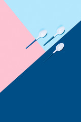Dangerous three plastic spoons. Environmental problem of plastic rubbish pollution. Three-color background: classic blue, pink and blue. Flat lay, top view, copy space.
