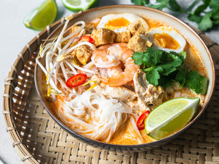 Malaysian noodles laksa soup with chicken, prawn and tofu in a bowl on grey background