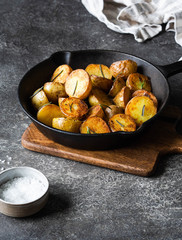 Black cast iron pan with fried roasted potato wedges with herbs on dark gray background