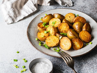 Fried roasted potato wedges with scallions on vintage plate on a gray background