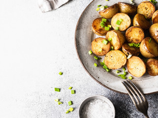 Fried roasted potato wedges with scallions on vintage plate on a gray background