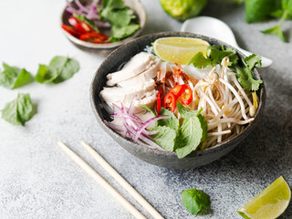Traditional Vietnamese soup- pho ga in bowl with chicken and rice noodles, mint and cilantro, red...