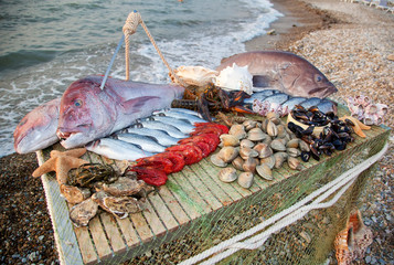 On the table are seafood: big fish, smaller fish, lobsters, mussels, oysters. The table stands on a...