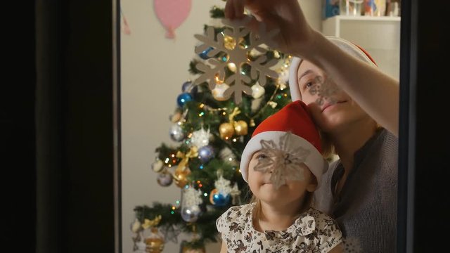 Mother and daughter on Christmas day glued to the window decorative snowflake