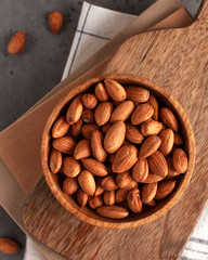 A handful of almonds on a wooden plate. Food photo on gray background. Healthy snack on the background of a wooden Board and a kitchen towel.