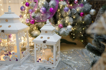 Big and little lanterns standing on the Christmas tree background. Fir decorated with purple baubles and garlands. New Year and winter holidays.