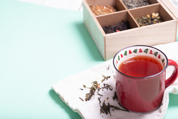 4 types of leaf tea of â€‹â€‹green, black, herbal with flowers and hearts in a tea box and a mug of black tea on a light background with copy space, top view