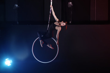 Young woman performing acrobatic element on aerial ring indoors © New Africa