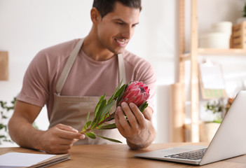 Florist with protea flower near laptop in floral store