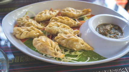 A dish of the tibetan fried momo with a sauce. Momo is a dish of dough with a filling.
