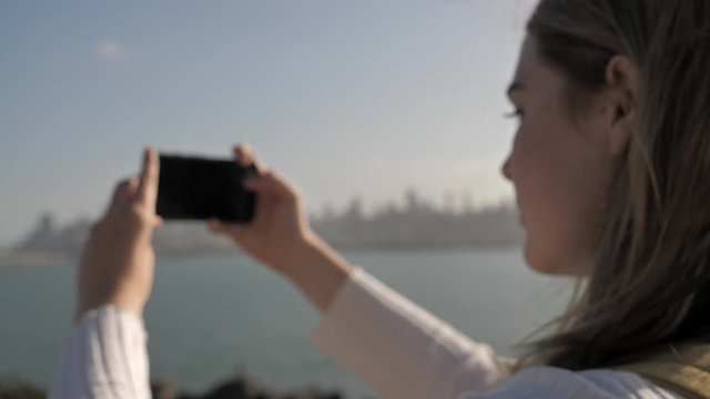 Young woman tourist taking photo with smartphone Alcatraz Island San Francisco