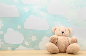 Teddy bear on white wooden table near wall with blue sky, space for text. Baby room interior