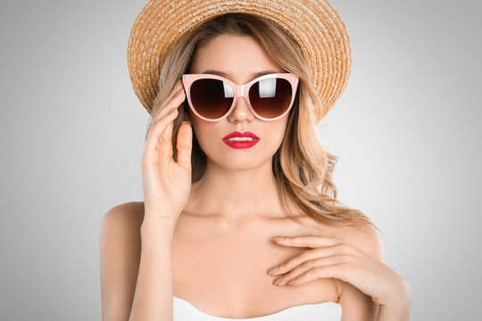 Young woman wearing stylish sunglasses and hat on light grey background