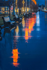 Rainy late evening in the park, a row of wooden benches, bright reflections of street lamps in wet...
