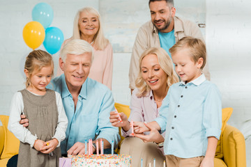 smiling mother and son holding candles near birthday cake, and family standing around