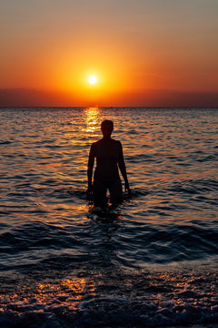 Young woman walking on water at sunset. Sunset and silhouette of a young woman as she emerges from the water.