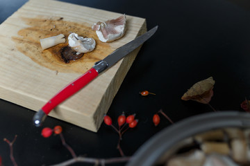 Fototapeta na wymiar Cut raw champignons in a metallic bowl standing on black wooden table. Сutting board, red knife with mushroom slices near. Healthy organic vegetarian food. Diet, nutrition concept. Copy space