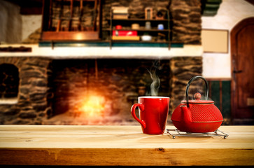 Metal kettle on wooden table.Free space for your decoration.Blurred background of fireplace with orange fire. Cold december night in home interior.Hot drink of tea,coffee or mulled.