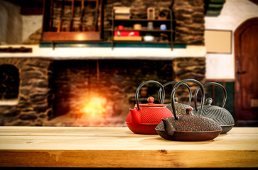 Metal kettle on wooden table.Free space for your decoration.Blurred background of fireplace with orange fire. Cold december night in home interior.Hot drink of tea,coffee or mulled.
