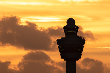 Amsterdam Schiphol International Airport control tower with a plane landing in the background during sunset. - obrazy, fototapety, plakaty