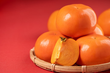 Fresh beautiful sliced sweet persimmon kaki isolated on red table background and bamboo sieve, Chinese lunar new year design concept, close up.