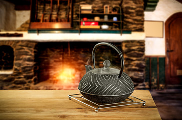 Metal kettle on wooden table.Free space for your decoration.Blurred background of fireplace with...