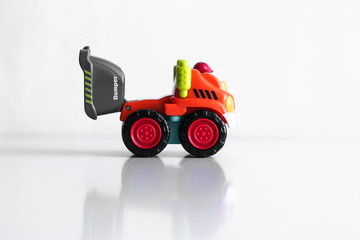 Plastic dump truck toy construction vehicle isolated on white background with reflection. Dumper side view. Orange vehicle with red wheels and name text. Operator in red hard hat